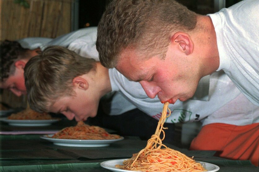 Junge Männer schlingeln Spaghetti ohne Besteck in sich rein