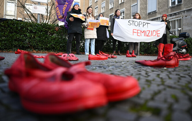 Teilnehmerinnen halten während des Hissens der Anti-Gewalt-Fahne anlässlich des Internationalen Tags für die Beseitigung von Gewalt gegen Frauen am Rathaus Tiergarten ein Banner mit der Aufschrift «Stoppt Femizide» hinter roten Schuhen
