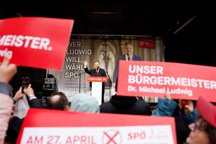 Im Hintergrund steht ein Mann an einem Rednerpult, im Saal werden Plakate mit der Aufschrift "Unser Bürgermeister Dr. Michael Ludwig" hochgehalten