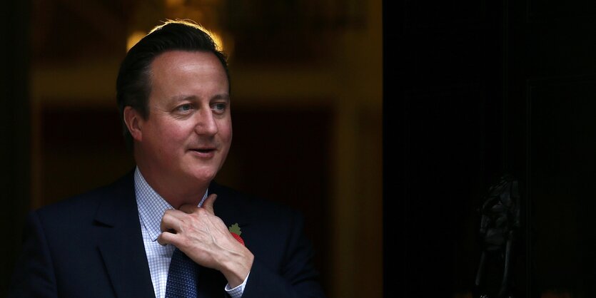 Mann an Anzug zupft sich an seiner Krawatte. Es ist der britische Premierminister David Cameron