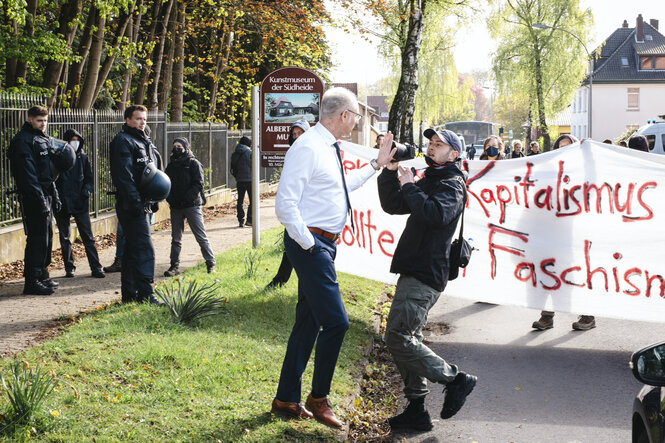 Ein Mann hält die Hand Richtung Kamera eines Fotografen, um ihn an seiner Arbeit zu hindern