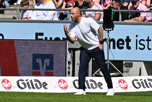 Lars Barlemann steht gestikulierend vor Werbebanden am Spielfeldrand