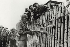 Eoldat verteilt Zigaetten an Menschen in Häftlingskleidung.