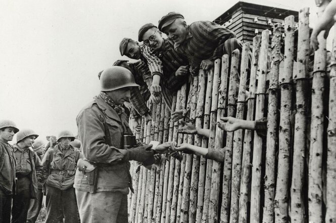 Eoldat verteilt Zigaetten an Menschen in Häftlingskleidung.
