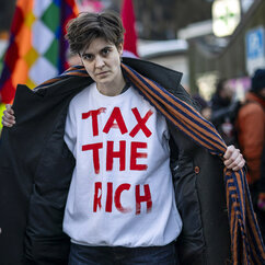 Zu sehen ist die Aktivistin Marlene Engelhorn mit geöffnetem Mantel und einem T-Shirt mit der Aufschrift "tax the rich".
