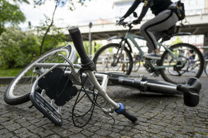 Ein Leihrad liegt mittig auf dem Gehweg. Ein Fahrradfaher fährt im Hintergrund an diesem vorbei.