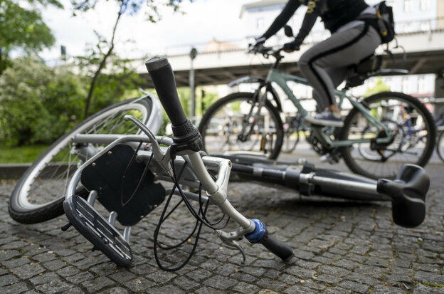 Ein Leihrad liegt mittig auf dem Gehweg. Ein Fahrradfaher fährt im Hintergrund an diesem vorbei.