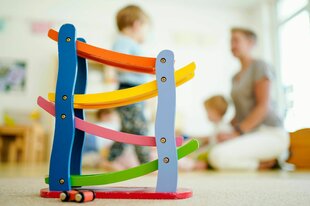 Eine Erzieherin spielt in einer Kindertagesstätte hinter einer Rollbahn mit Kindern