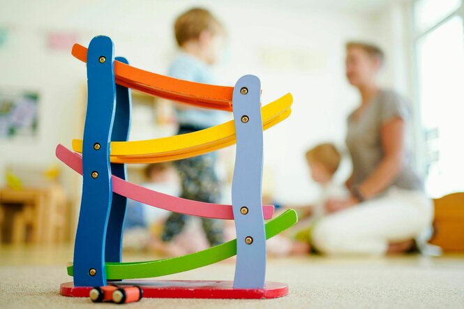 Eine Erzieherin spielt in einer Kindertagesstätte hinter einer Rollbahn mit Kindern