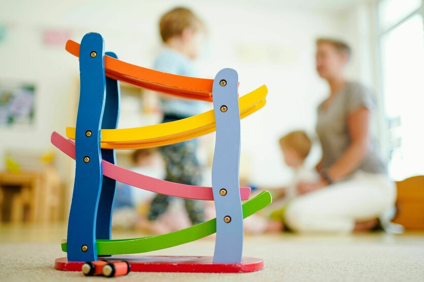 Eine Erzieherin spielt in einer Kindertagesstätte hinter einer Rollbahn mit Kindern