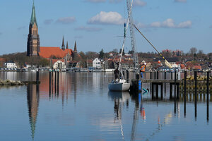Stadtansicht von Schleswig quer über die Schlei, auf deren ruhiger Wasseroberfläche sich Kirchturm und Häuser spiegeln