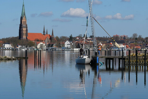 Stadtansicht von Schleswig quer über die Schlei, auf deren ruhiger Wasseroberfläche sich Kirchturm und Häuser spiegeln