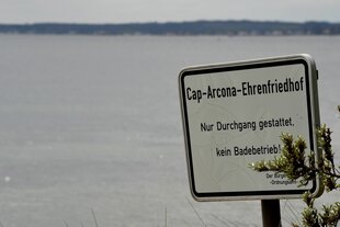 Ein Schild am Rand der Ostsee weist einen Strandabschnitt als Ehrenfriedhof aus, an dem Baden verboten ist