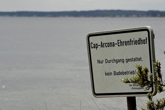 Ein Schild am Rand der Ostsee weist einen Strandabschnitt als Ehrenfriedhof aus, an dem Baden verboten ist