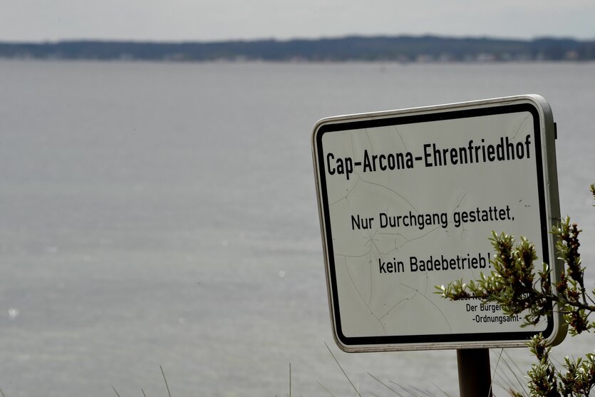Ein Schild am Rand der Ostsee weist einen Strandabschnitt als Ehrenfriedhof aus, an dem Baden verboten ist