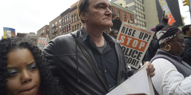 Demonstration in New York, in der Mitte ein weißer Mann in Lederjacke, Quentin Tarantino, links und rechts von ihm schwarze Frauen