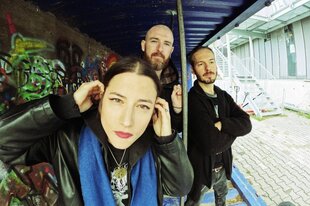 Die Mitglieder der Band Crashpad stehen unter einem Unterstand auf einem industriellen Hinterhof. Die Wand hinter ihnen ist mit Graffiti bemalt.