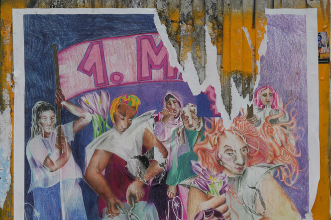 Ein zerrissenes Plakat an einer Hauswand, auf dem zum feministischen Block auf dem 1. Mai aufgerufen wird. Dargestellt ist eine Frau, die Stacheldraht durchtrennt