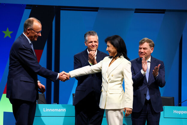 Friedrich Merz und Katherina Reiche stehen auf einer Bühne und schütteln die Hände, im Hintergrund applaudieren zwei Männer