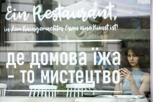 Eine junge Frau sitzt mit ihrem Handy in der Hand in einem Restaurant hinter der Schaufensterscheibe