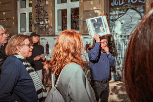 Ein Mann, umringt von einer Gruppe Menschen hält bei einer Führung ein Schwarz-Weiß Bild von Gustav Landauer hoch