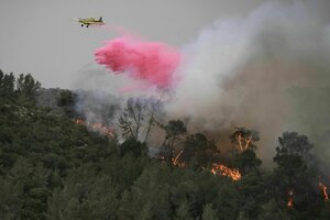 Ein kleines Flugzeug fliegt über brennendem Wald und hinterlässt eine rosa Wolke aus Löschmitteln