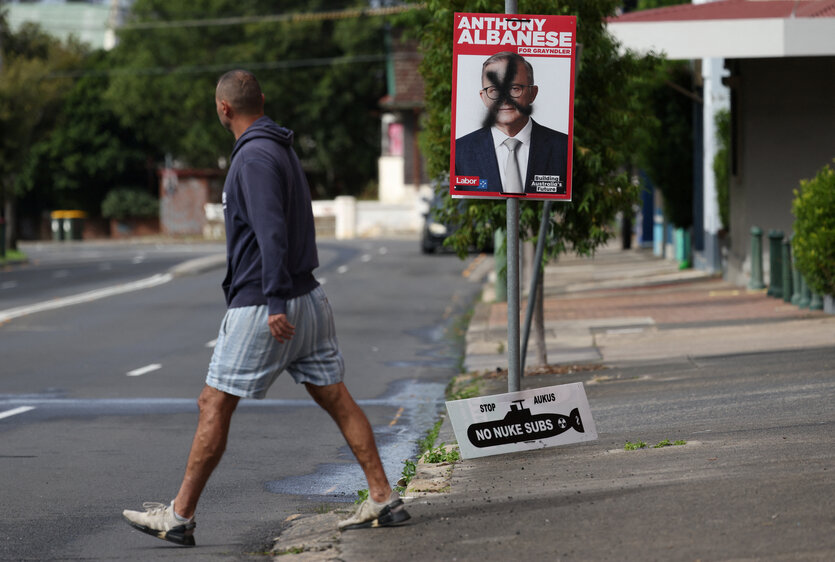 Ein Mann läuft auf der Straße an einem beschmierten Wahlplakat vorbei.