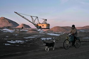 Eine Frau, begleitet von ihrem Hund an einem Seilbagger vorder, der Seltene Erden abbaut