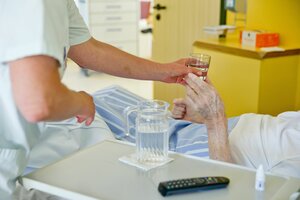 Eine Krankenpflegerin reicht einem Patienten ein Glas Wasser.