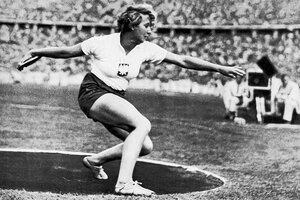 ein altes Foto mit einer Frau beim Diskuswurf in einem vollen Stadion