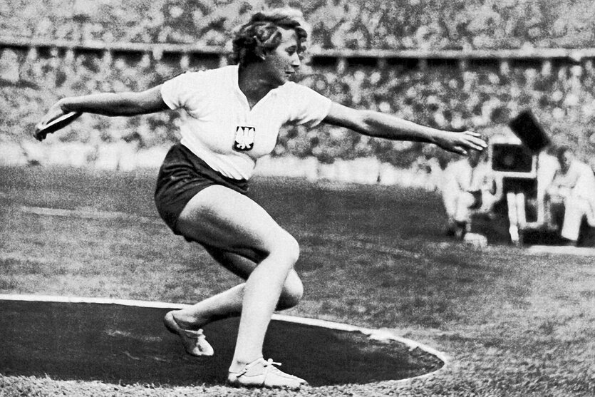 ein altes Foto mit einer Frau beim Diskuswurf in einem vollen Stadion