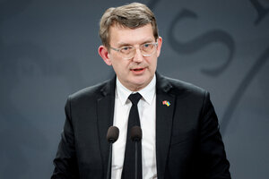 Ein Mann mit schwazem Jacket steht an einem Rednerpult und spricht ins Mikrofon