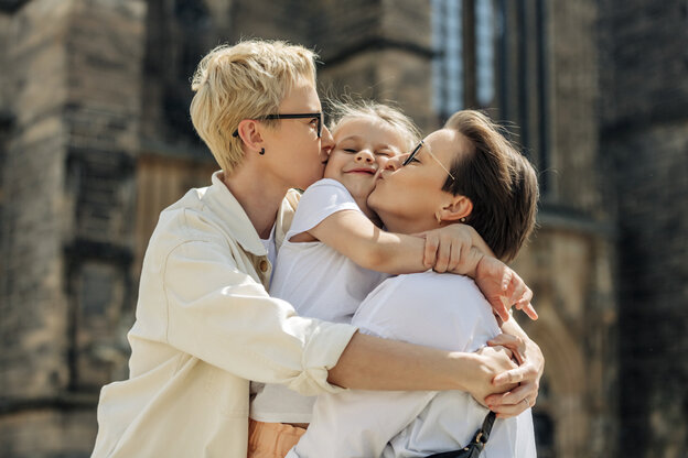 Zwei Frauen umarmen ein Mädchen und küssen es beide auf die Wangen