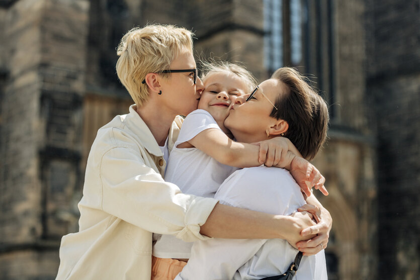 Zwei Frauen umarmen ein Mädchen und küssen es beide auf die Wangen