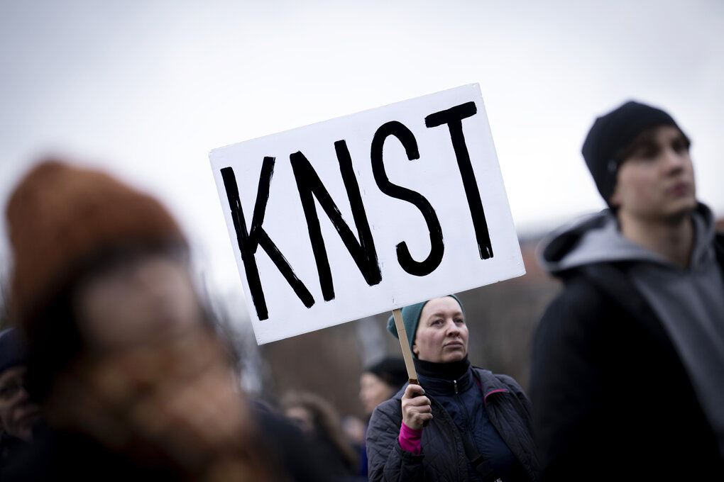 Demonstrierende halten ein Protestschild in die Höhe, auf dem steht: KNST