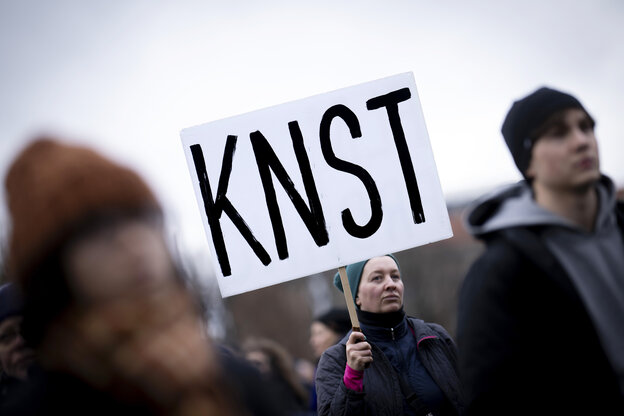 Demonstrierende halten ein Protestschild in die Höhe, auf dem steht: KNST