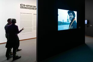 Besucher der Neuen Nationalgalerie stehen in der Ausstellung «Deutschland '99» von Christoph Schlingensief, rechts läuft in Endlosschleife das Video zur Dokumentation der Aktion «Deutschland versenken» aus dem Jahr 1999