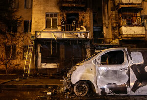 Ein völlig zerstörtes Auto vor einer verkohlten Häuserfassade in der Nacht