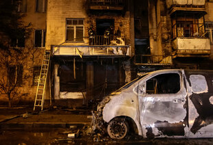 Ein völlig zerstörtes Auto vor einer verkohlten Häuserfassade in der Nacht