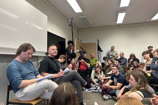 Referent Ingar Solty und Linken-Politiker Cem Ince in einem Seminarraum, in dem sich viele Menschen drängen