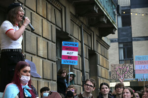 Eine Person hält vor einem Gebäude eine Rede, während viele andere Menschen darum herum stehen und Plakate mit Unterstützung für trans Personen halten