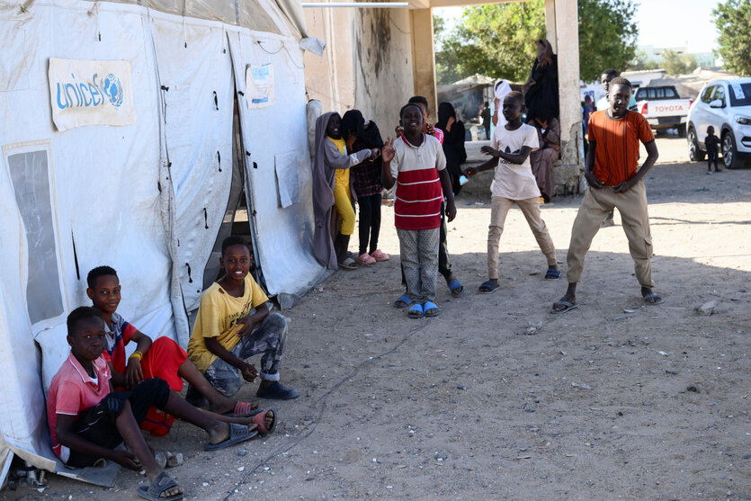 Kinder sitzen vor einem mit Planen verhängten Gebäude mit der Aufschrift Unicef