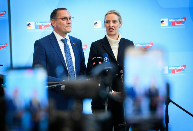 AfD-Chefs Tino Chrupalla und Alice Weidel vor blauem Hintergrund mit AfD-Logos
