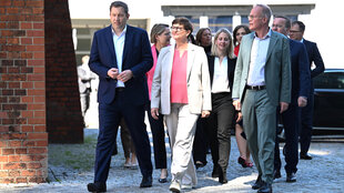 Lars Klingbeil und die frisch gekürten MinisterInnen der SPD gehen gemeinsam bei sonnigem Wetter an einer Backsteinwand