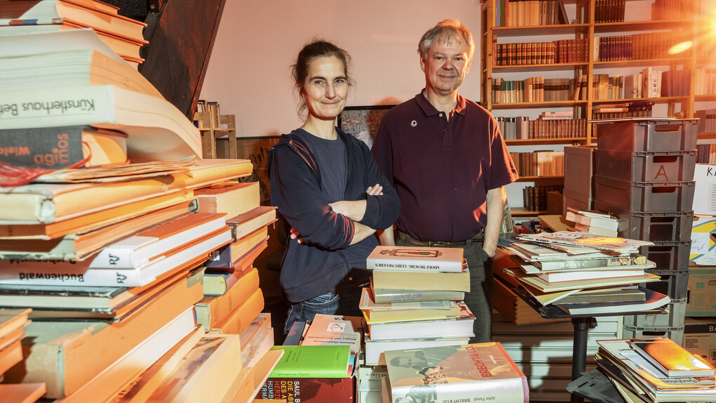 Esther Winkelmann und Juergen Repschlaeger stehen in ihrem Aantifaschistischen Antiquariat, umgeben von Büchern in Regalen und auf Stapeln