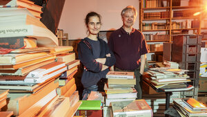 Esther Winkelmann und Juergen Repschlaeger stehen in ihrem Aantifaschistischen Antiquariat, umgeben von Büchern in Regalen und auf Stapeln