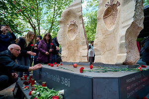 Zu sehen ist das Denkmal im geöffneten Zustand und menschen die Blumen niederlegen