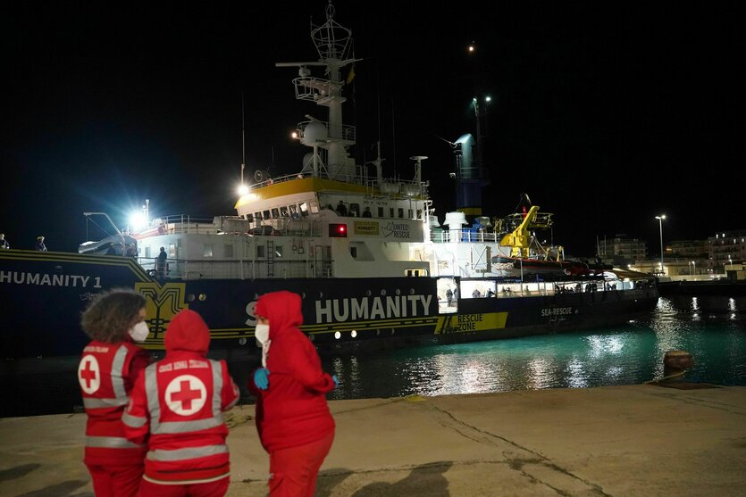 Das humanitäre Schiff «SOS Humanity 1» liegt im Hafen vor Anker, drei Personen in Rot Kreuz Kleidung stehen im Vordergrund