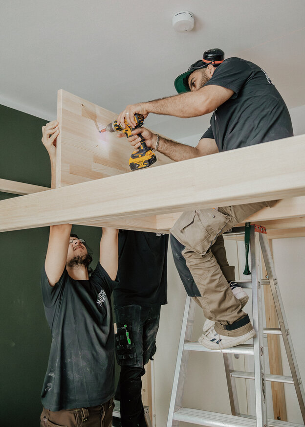 Zwei Männer verschrauben Holzleisten für ein Hochbett