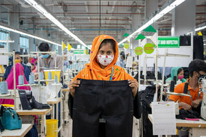 Eine Textilarbeiterin in Bangladesh steht in einer Fabrik und hält eine Hose vor sich
